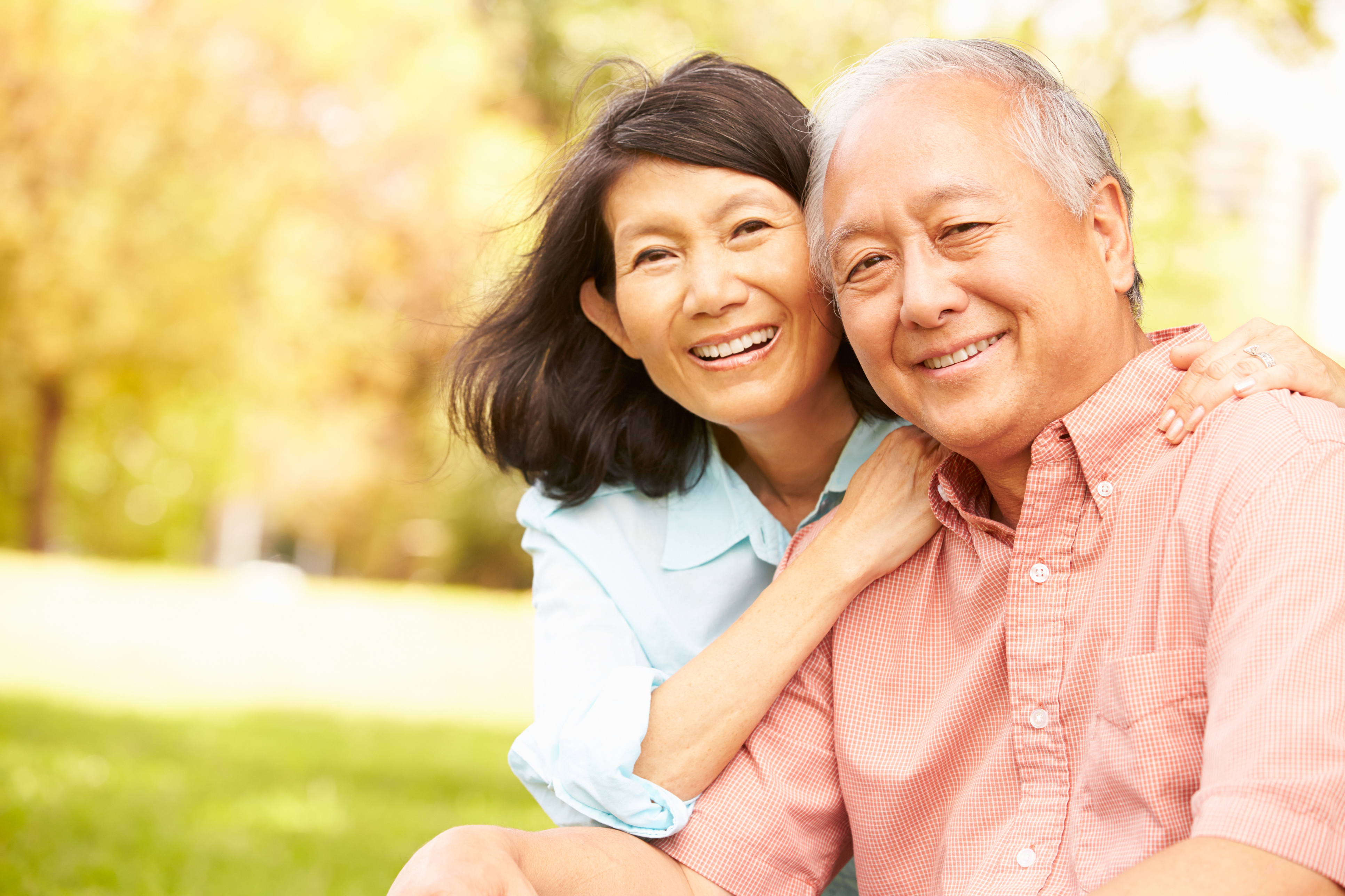 Portrait Of Senior Asian Couple Sitting In Park Together Smiling To Camera