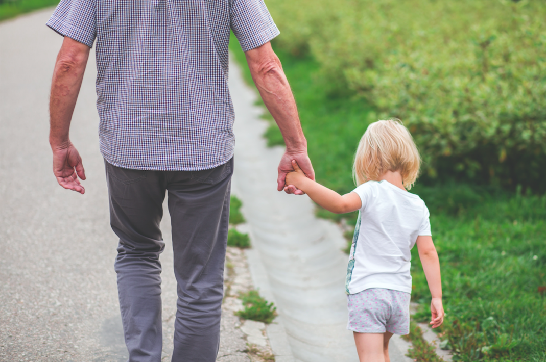 grandparent walking outside and holding hand with young child